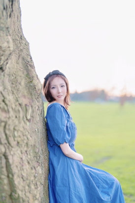 Pretty Korean girl in a blue dress leaning against a tree