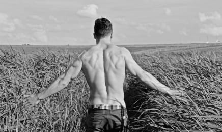 Fit topless man walking in a wheat field