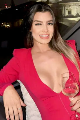 Smiling Brazilian girl in a revealing pink jacket holding a glass of wine